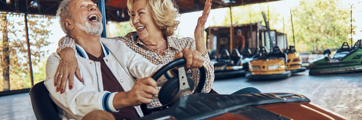 An older couple laughing while riding bumper cars at a carnival.
