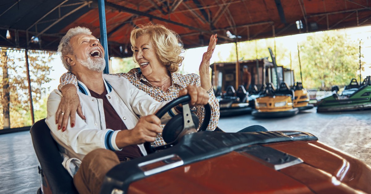 An older couple laughing while riding bumper cars at a carnival.