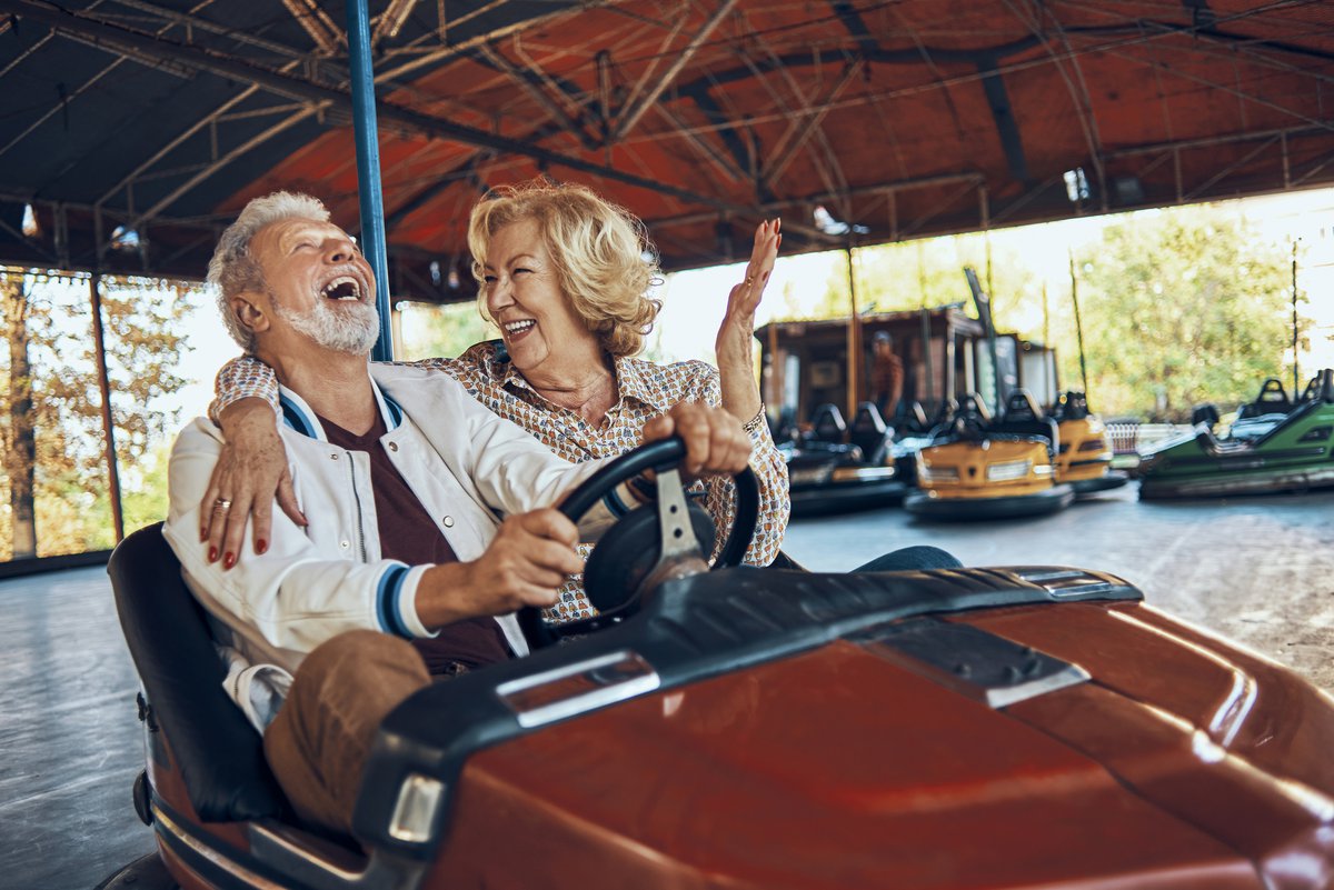 An older couple laughing while riding bumper cars at a carnival.