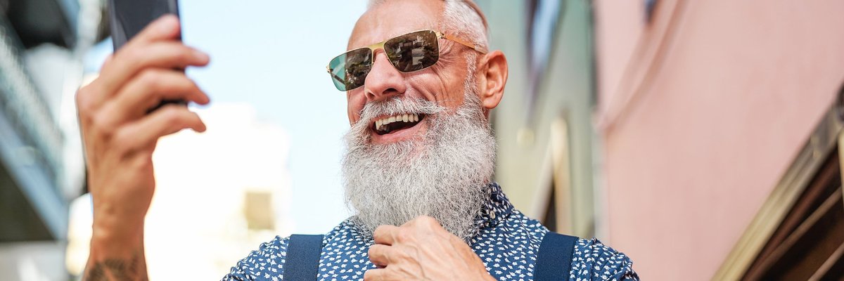 An older man with a long gray beard and tattoos taking a selfie.