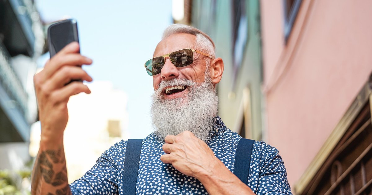 An older man with a long gray beard and tattoos taking a selfie.