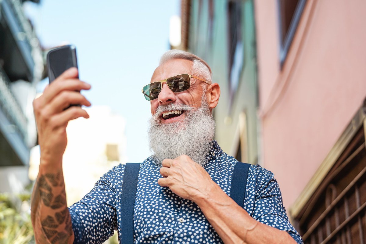 Un homme plus âgé avec une longue barbe grise et des tatouages ​​prenant un selfie.