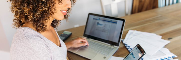 A woman looking at her finances with a laptop and phone.