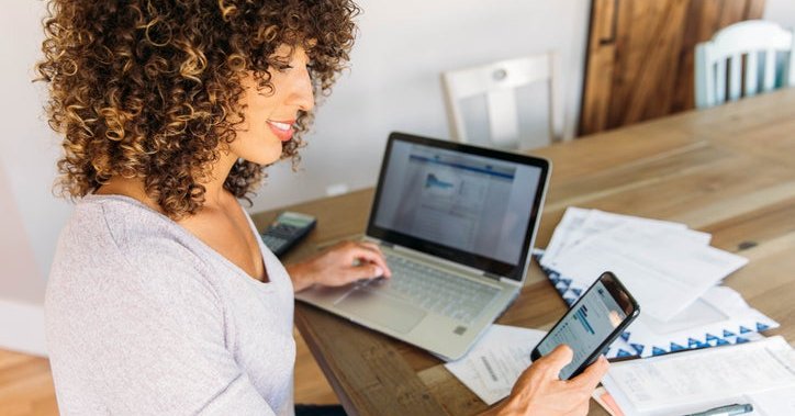 A woman looking at her finances with a laptop and phone.