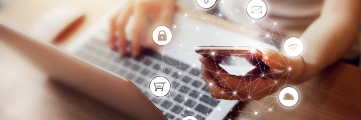 Woman sitting in front of a laptop and holding a cell phone with banking icons floating around her hand