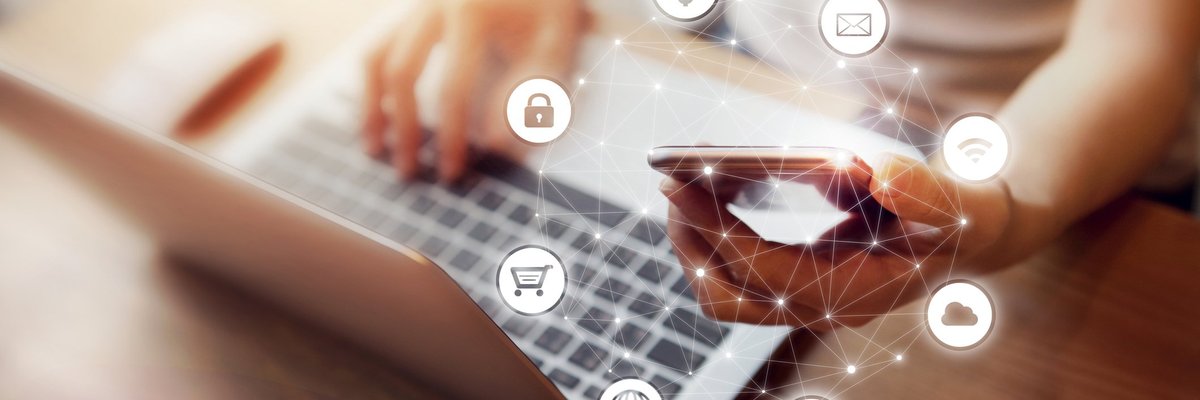 Person looking at laptop and holding mobile phone with cloud of financial symbols above phone