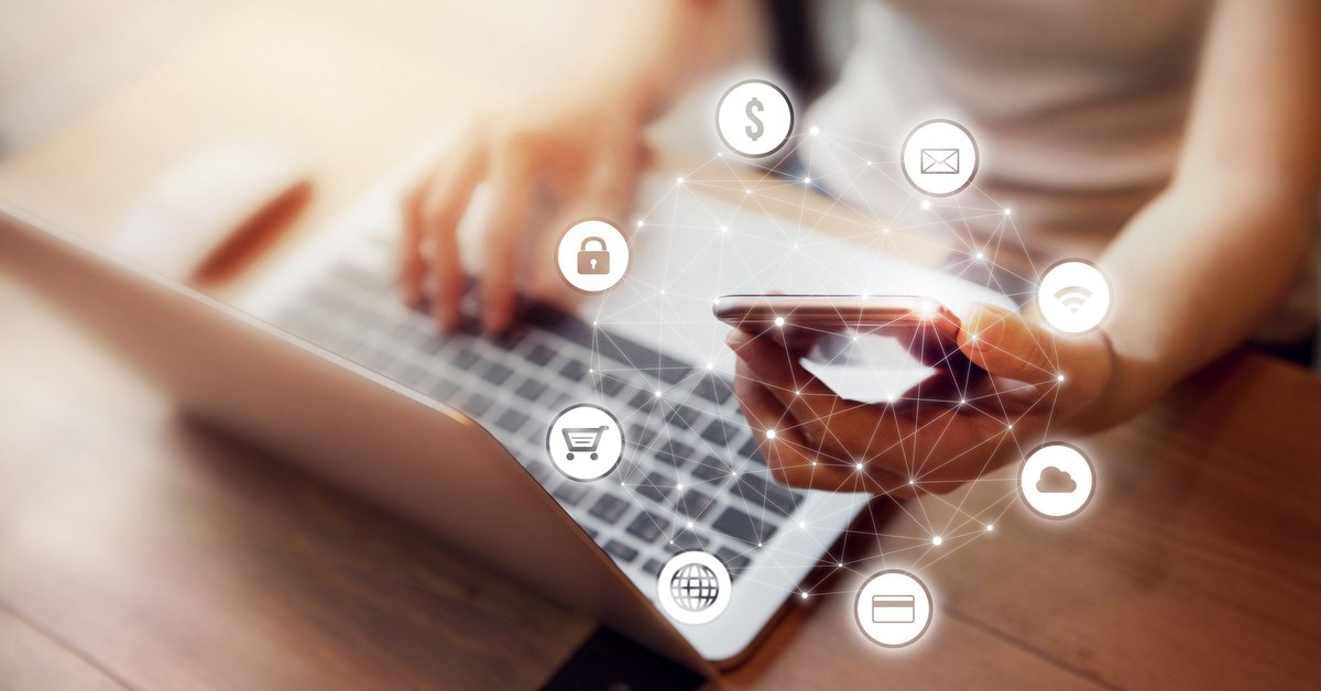Woman sitting in front of a laptop and holding a cell phone with banking icons floating around her hand