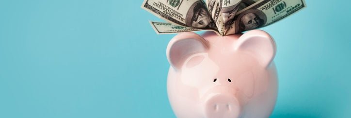 A piggy bank with hundred-dollar bills sticking out the top.
