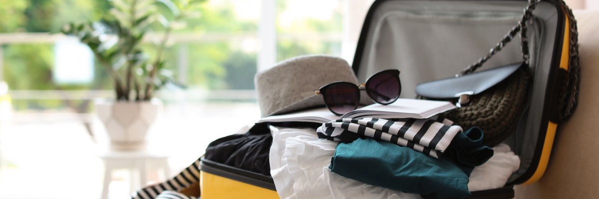 A suitcase packed with clothes sitting open in front of a sunny window.