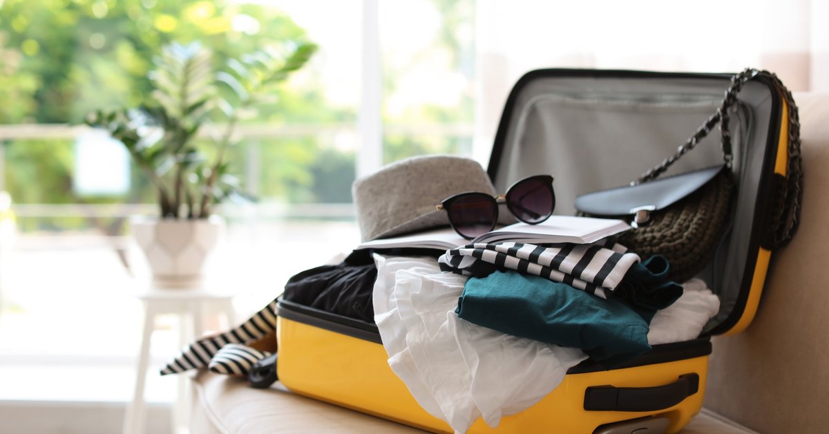 A suitcase packed with clothes sitting open in front of a sunny window.