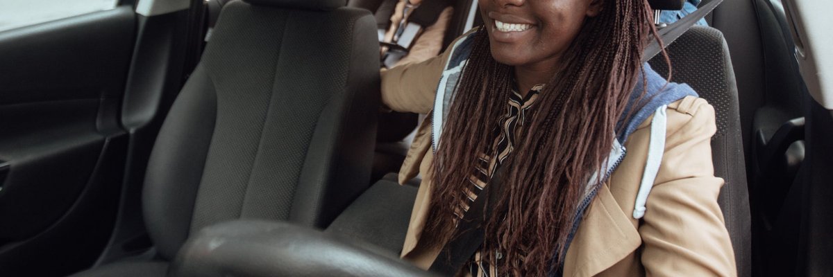 A smiling parent driving a car with their two kids in the backseat.
