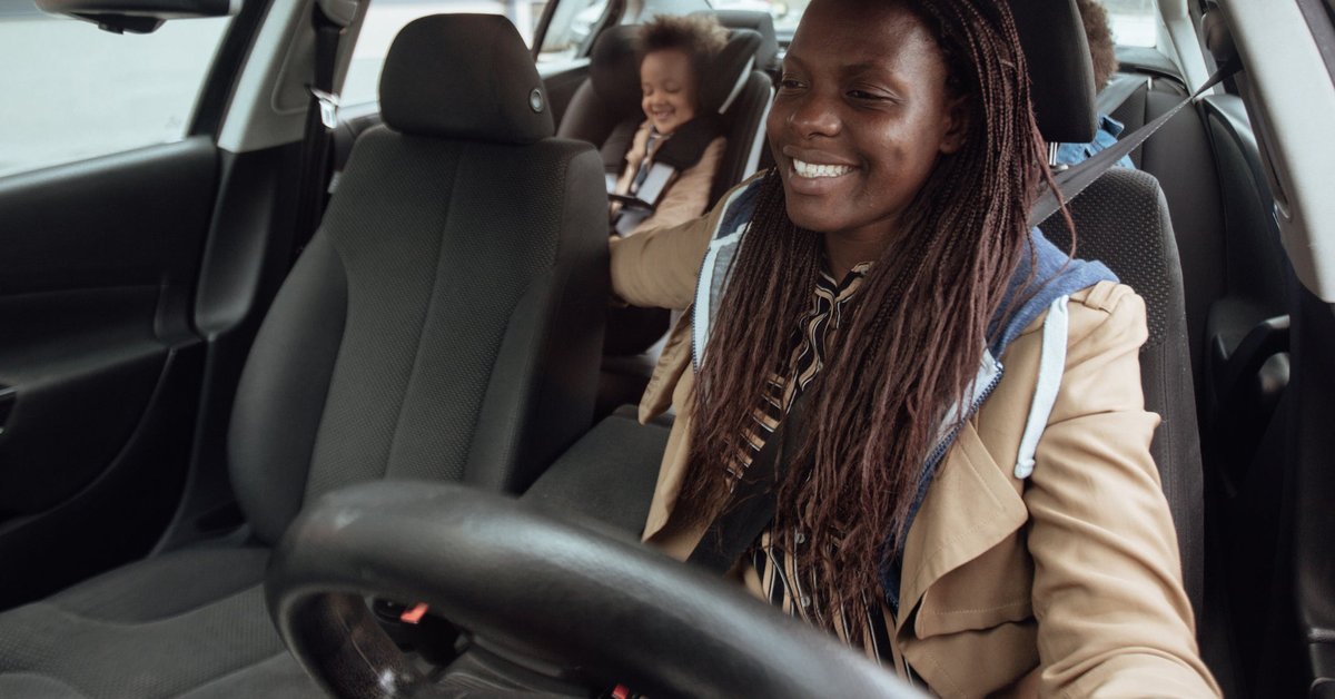 A smiling parent driving a car with their two kids in the backseat.