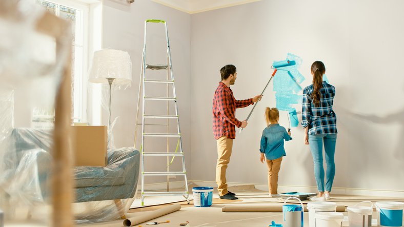 A mom, dad, and their young daughter painting the wall of their living room blue.