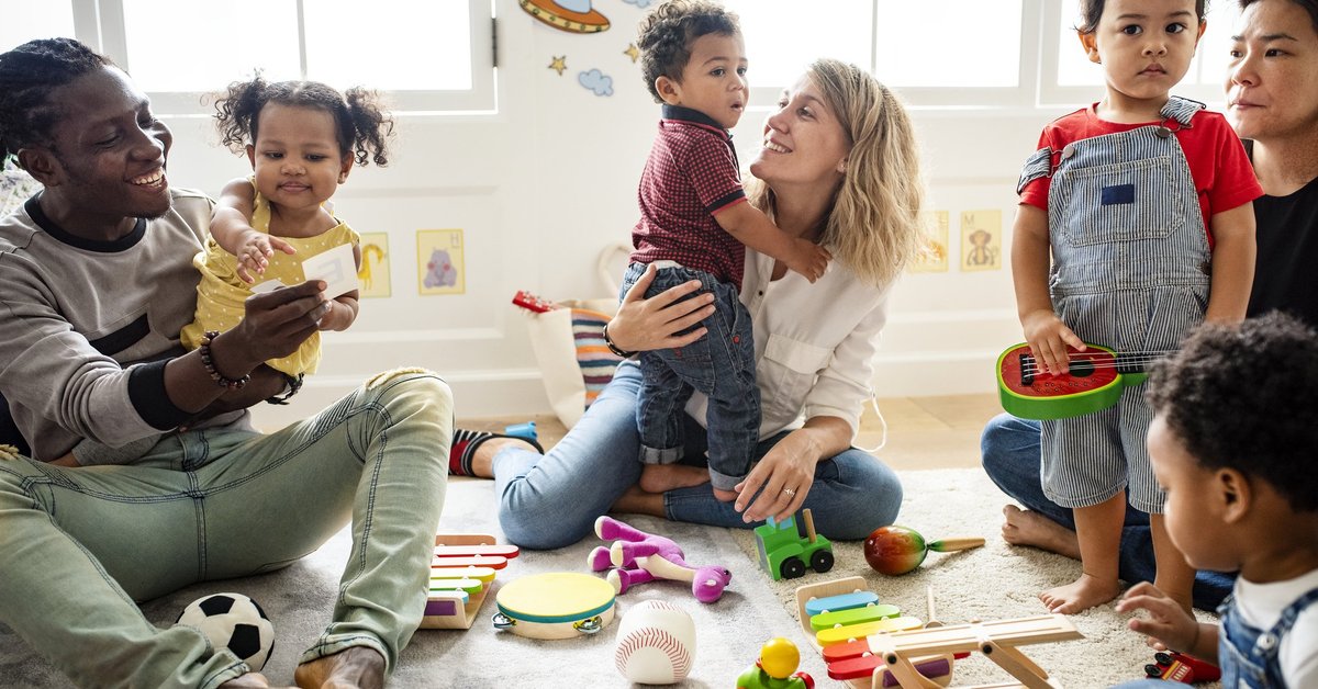Smiling parents playing with their young children in a preschool classroom.