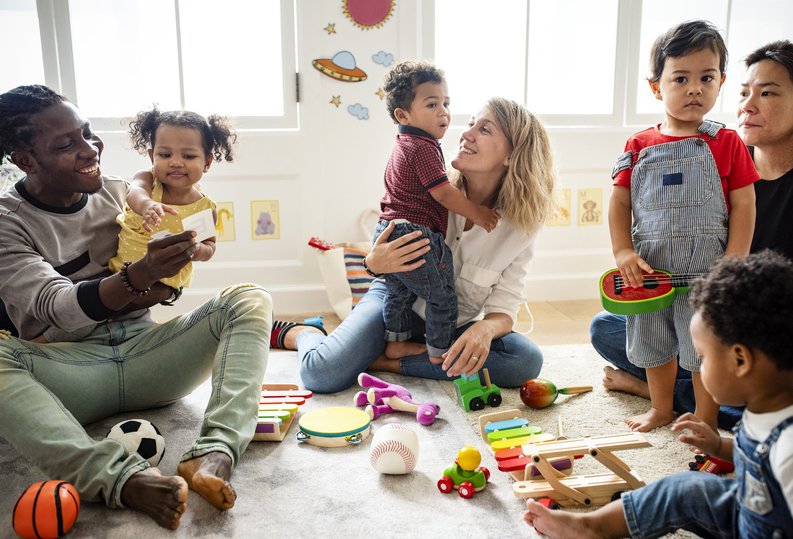 Smiling parents playing with their young children in a preschool classroom.