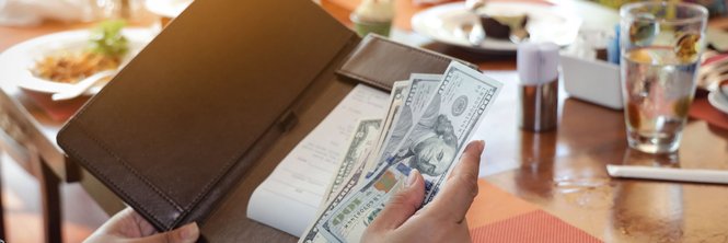 A woman placing cash in a check folder while sitting at a table in a restaurant.