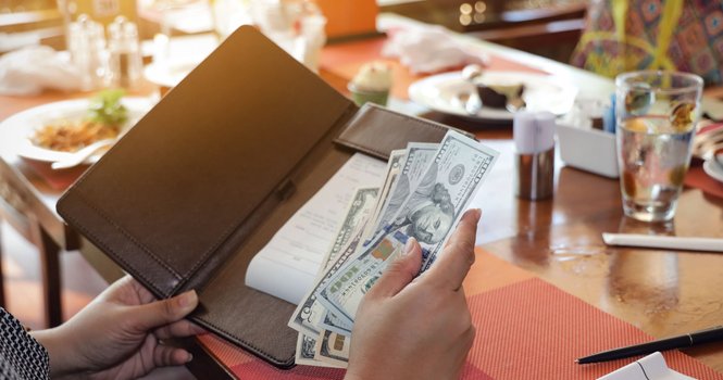 A woman placing cash in a check folder while sitting at a table in a restaurant.