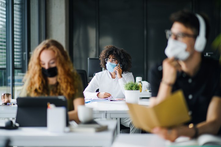 Three people wearing medical masks while seated apart and working in an office.