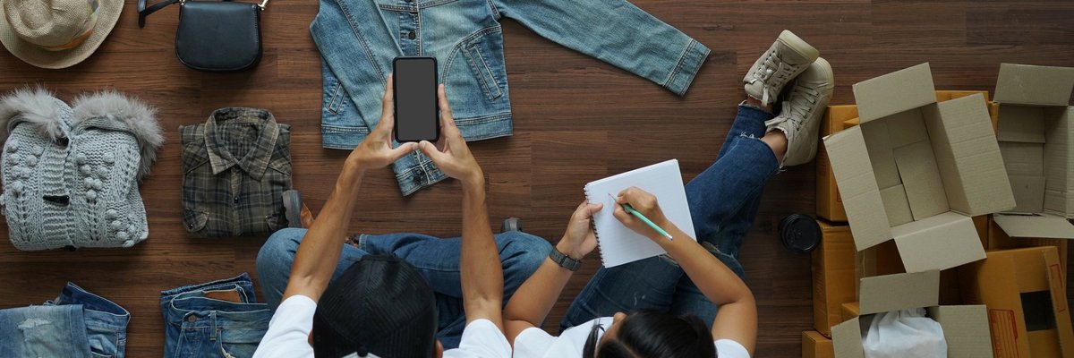 Two people sitting on the floor and taking pictures of their used clothes to sell.