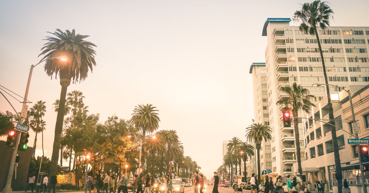 People crossing a city street in Los Angeles that's lined with palm trees.