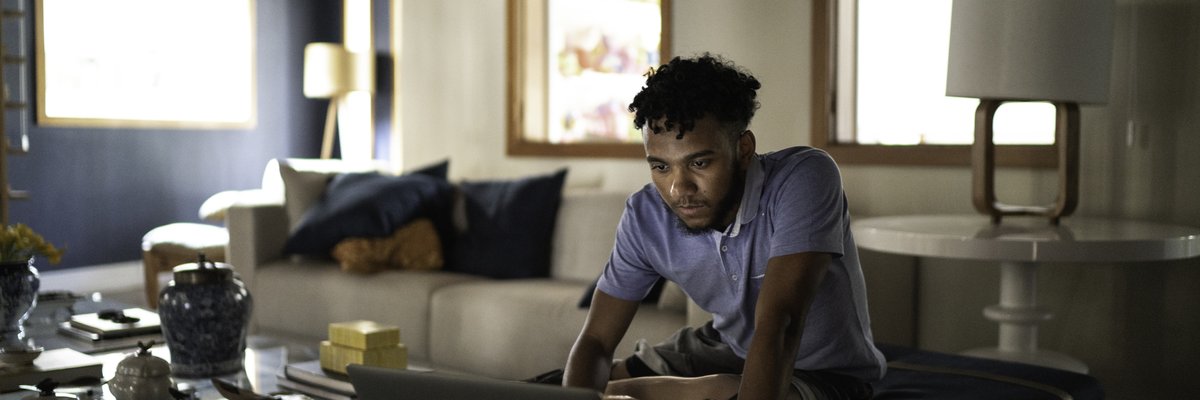 A person sitting on their couch at home and typing on a laptop.
