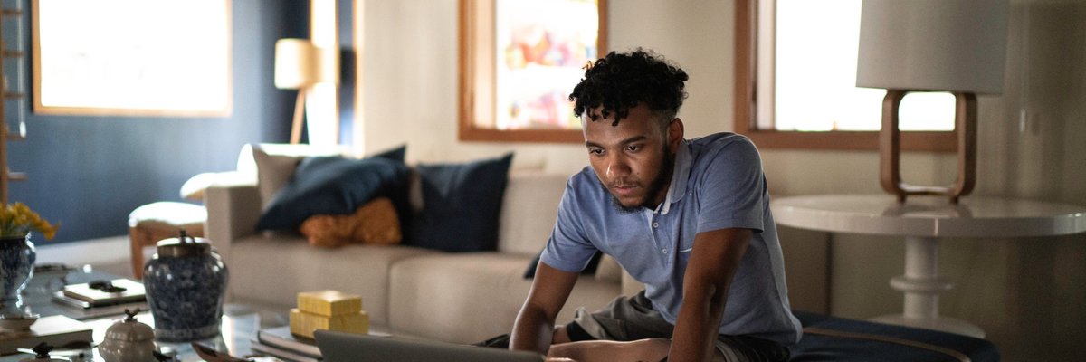 A person sitting on their couch at home and typing on a laptop.