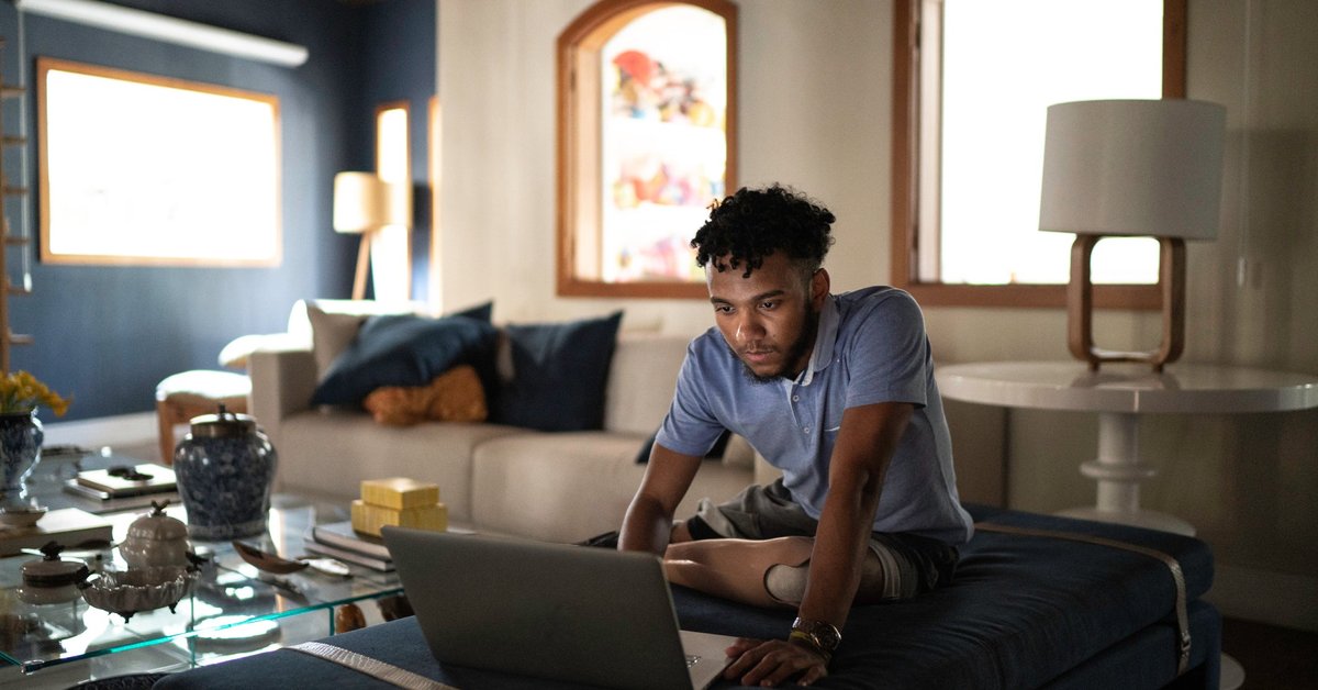 A person sitting on their couch at home and typing on a laptop.