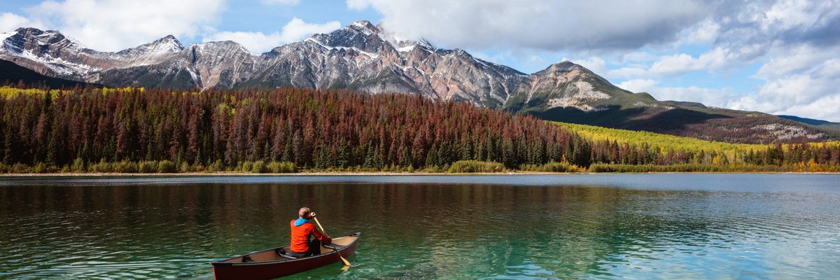 A person paddling a canoe across a clear blue lake surrounded by mountains in Canada.