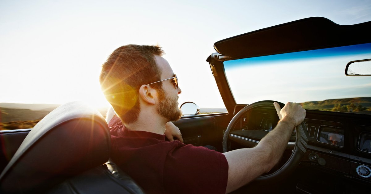 A person driving a convertible car with the top down and the sun shining.