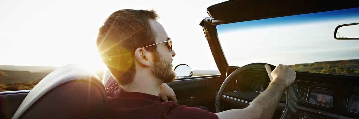 A person driving a convertible car with the top down and the sun shining.