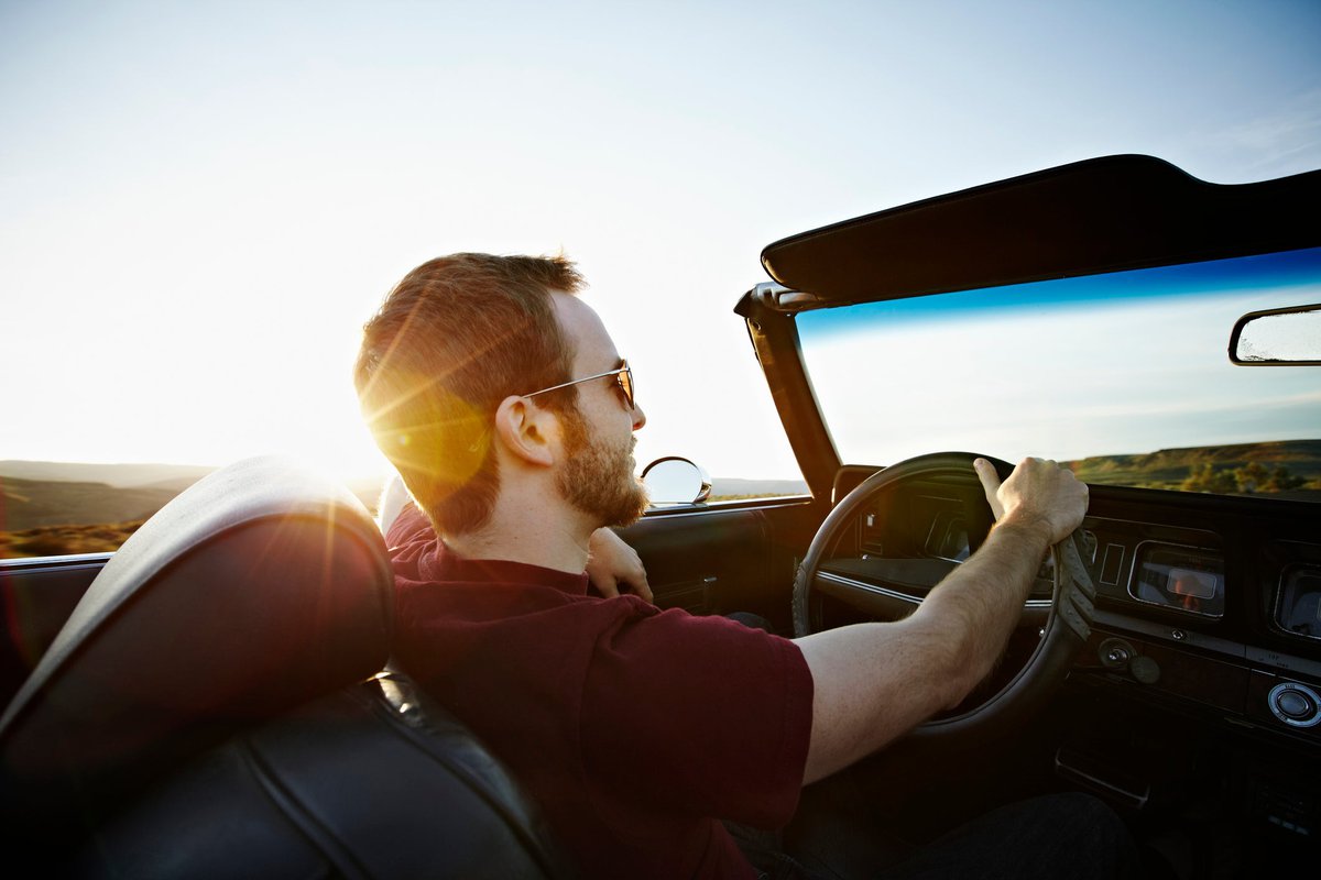 A person driving a convertible car with the top down and the sun shining.