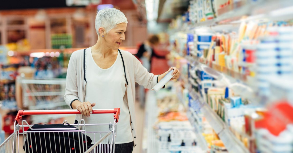 A person with a shopping cart looking at a refrigerated item in a grocery store.
