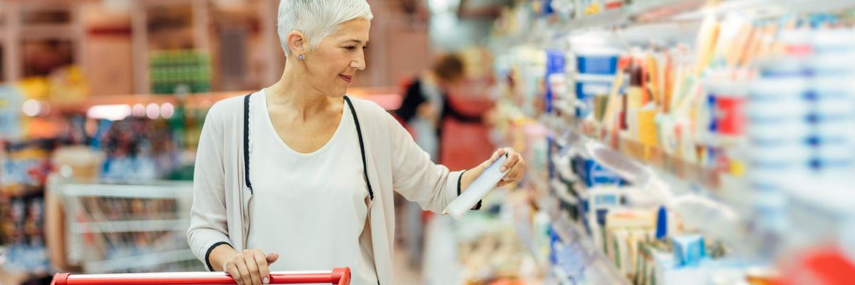 A person with a shopping cart looking at a refrigerated item in a grocery store.