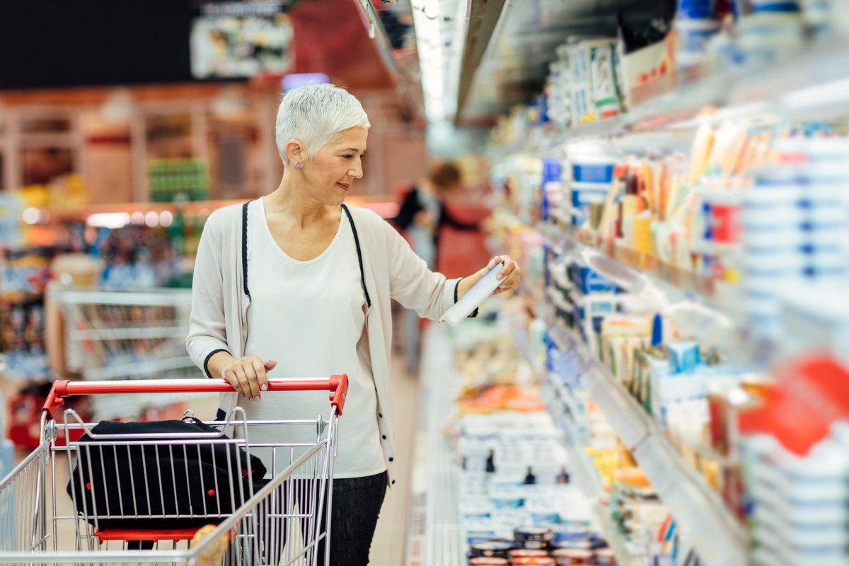 A person with a shopping cart looks at a refrigerated item in a grocery store.