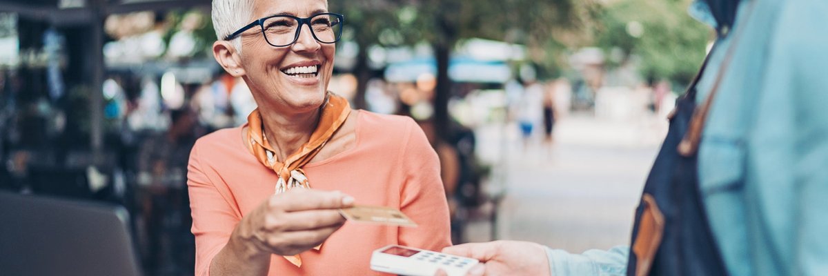 A person sitting at an outdoor table handing a credit card to a restaurant employee holding a payment reader.