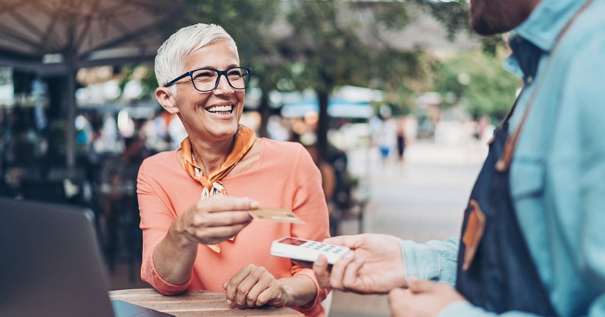 A person sitting at an outdoor table handing a credit card to a restaurant employee holding a payment reader.