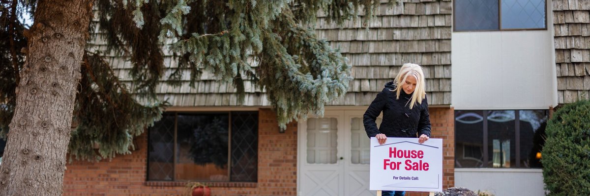A person putting a House for Sale sign in the front lawn of their property.