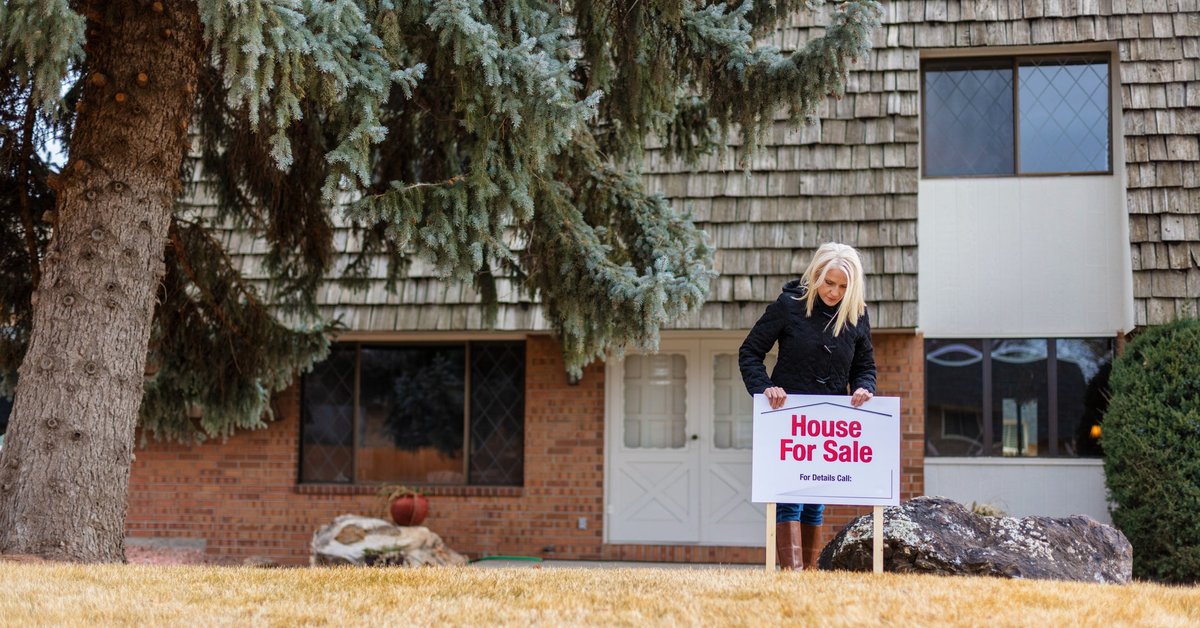 A person putting a House for Sale sign in the front lawn of their property.