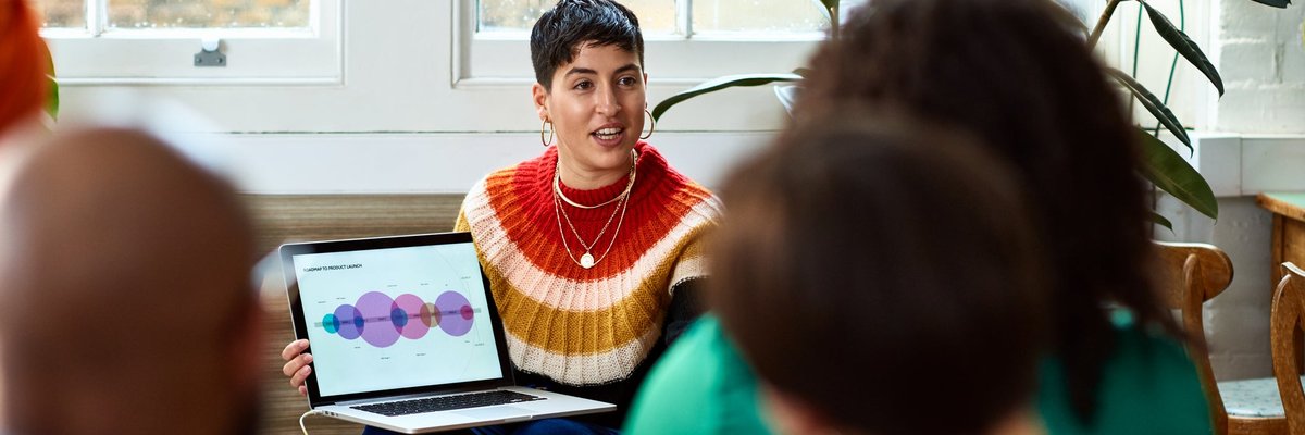 A person holding a laptop and leading a meeting in an office.