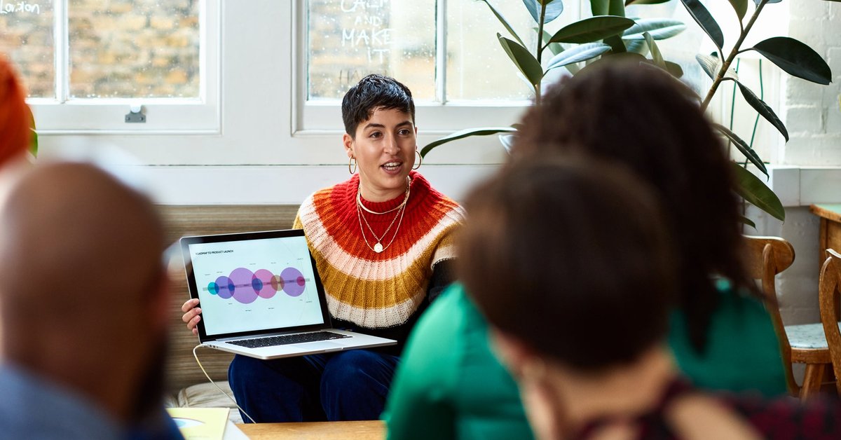 A person holding a laptop and leading a meeting in an office.