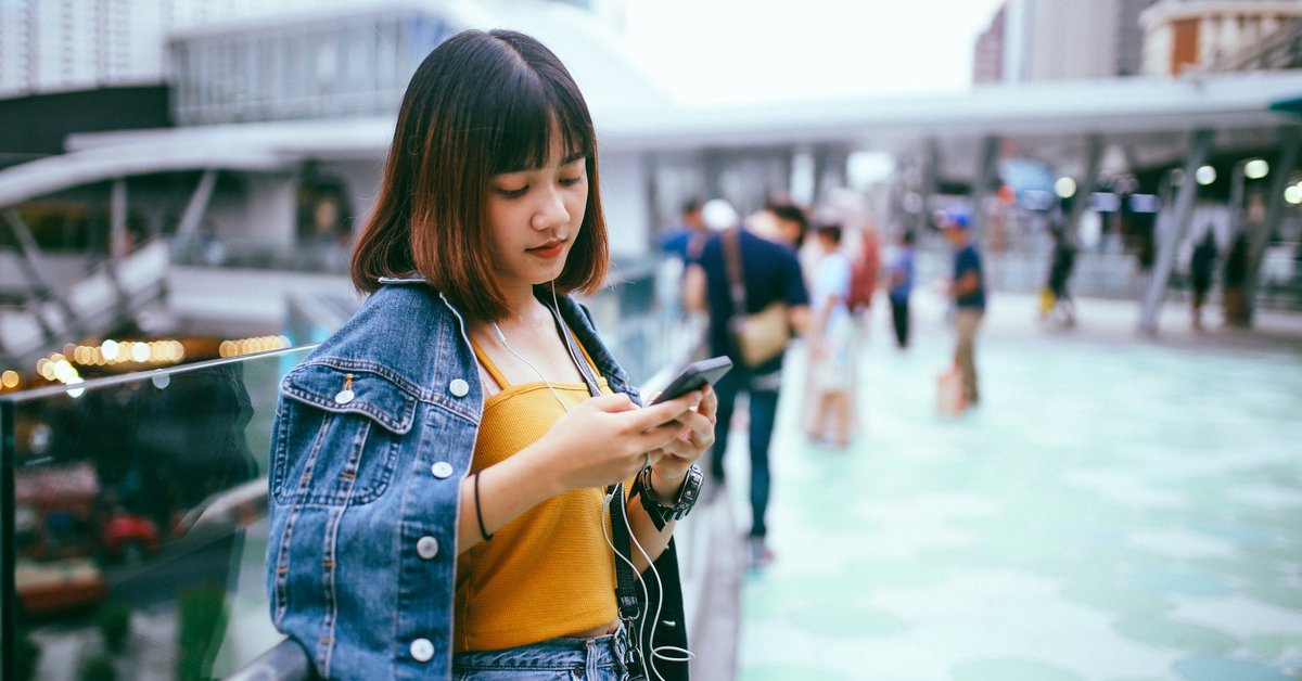A person leaning against a railing in a busy city center while looking at a cell phone.