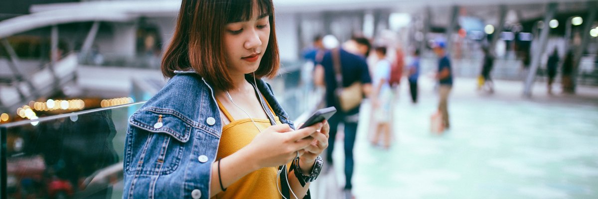 A person leaning against a railing in a busy city center while looking at a cell phone.