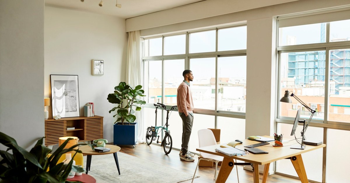 A person standing and looking out the window of their apartment.