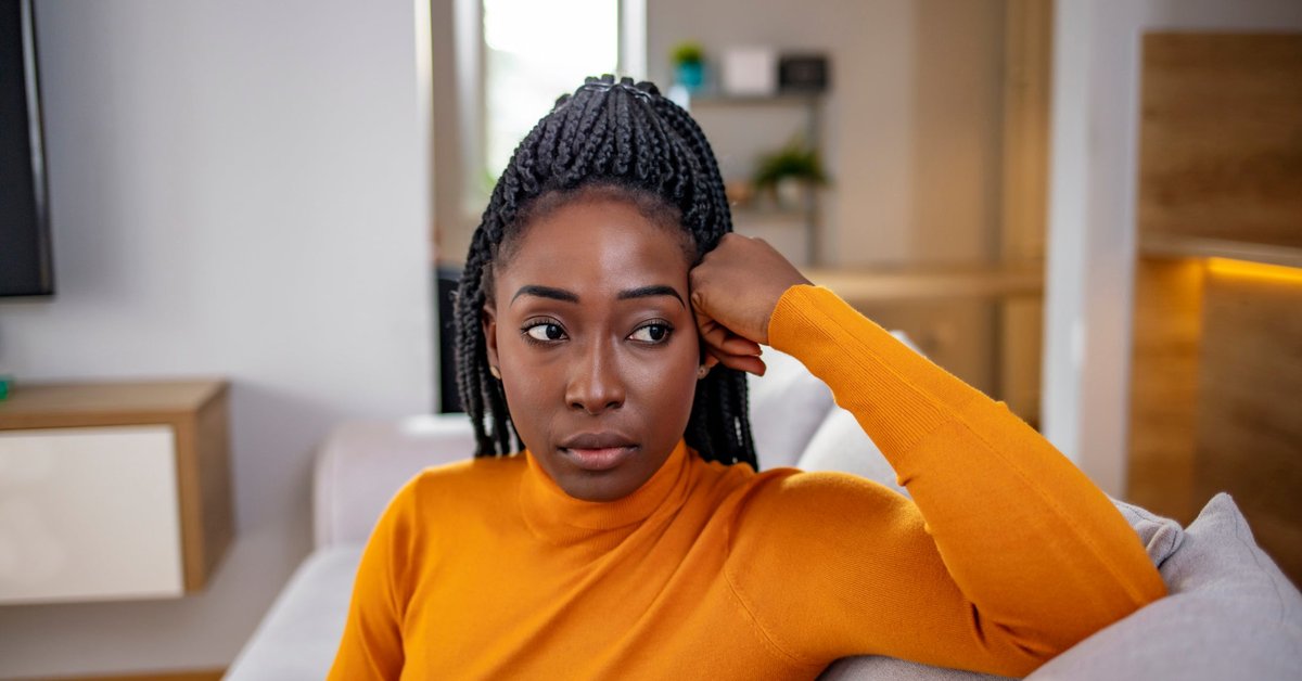 A person looking stressed and thoughtful while sitting on their couch.