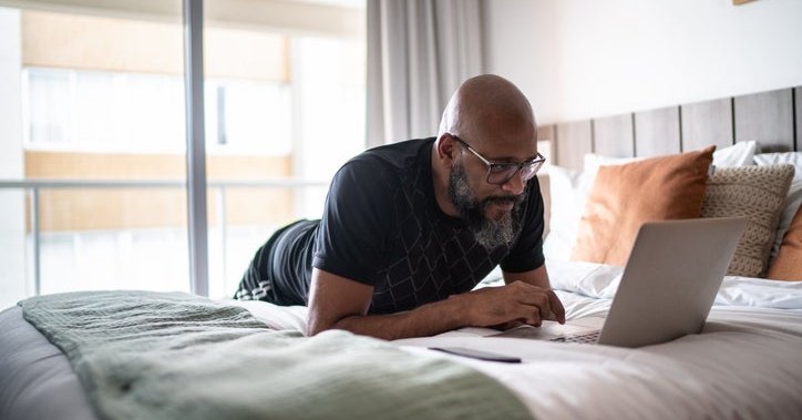 A person lying on a bed while searching on a laptop.