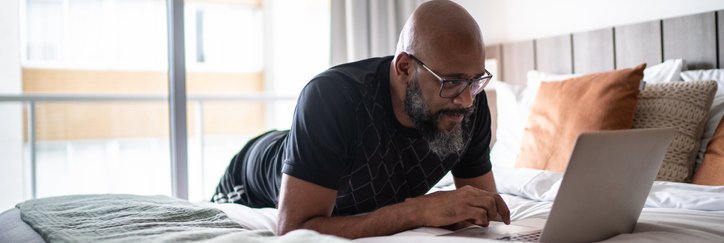 A person lying on a bed while searching on a laptop.