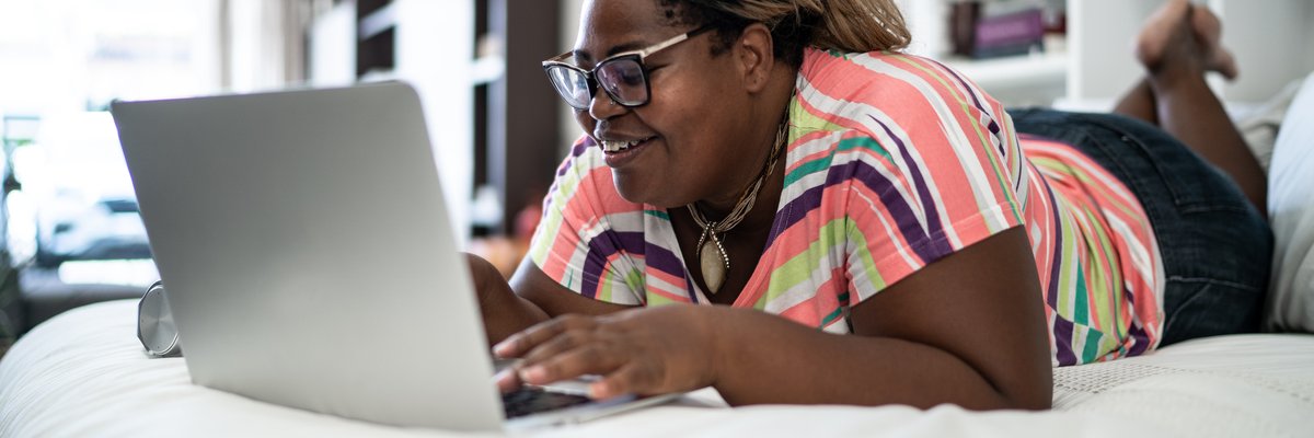 A smiling person lying on a bed while searching on a laptop.