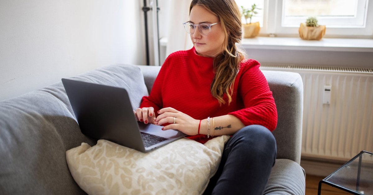 A person typing on a laptop while sitting comfortably on a couch.