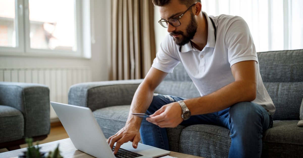 A person sitting on the couch and holding a credit card in one hand while typing on a laptop.