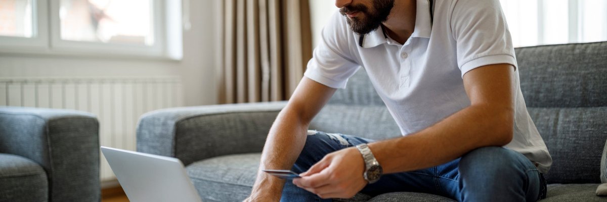 A person sitting on the couch and holding a credit card in one hand while typing on a laptop.